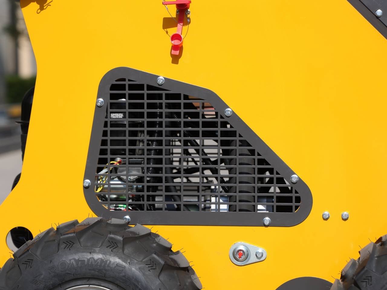 Close-up of a yellow off-road vehicle side panel with a safety red lanyard and a vented engine compartment behind a black grille.