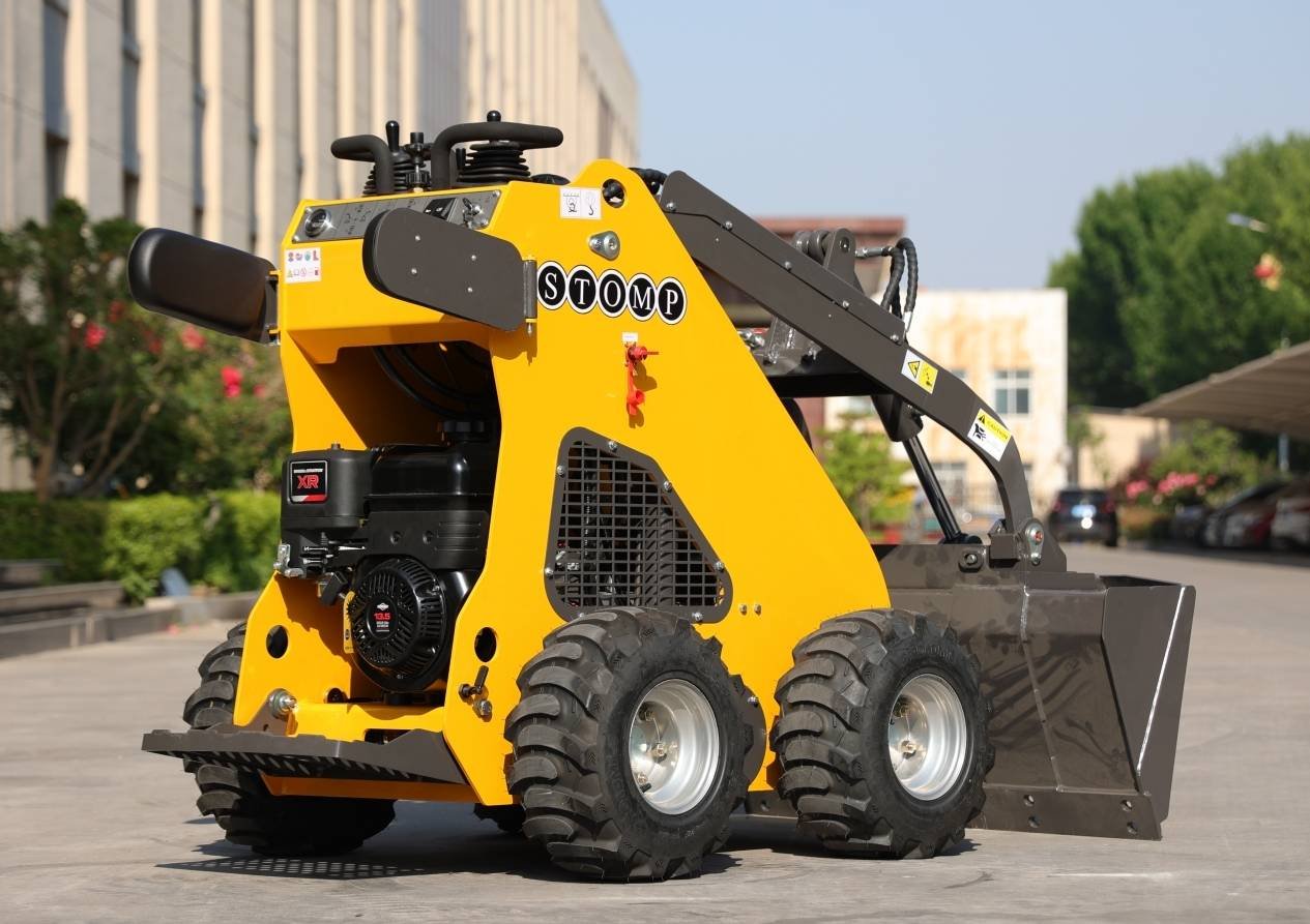 Yellow compact loader with black hydraulic arms and a front bucket parked on a paved lot, STOMP branding visible on the side.