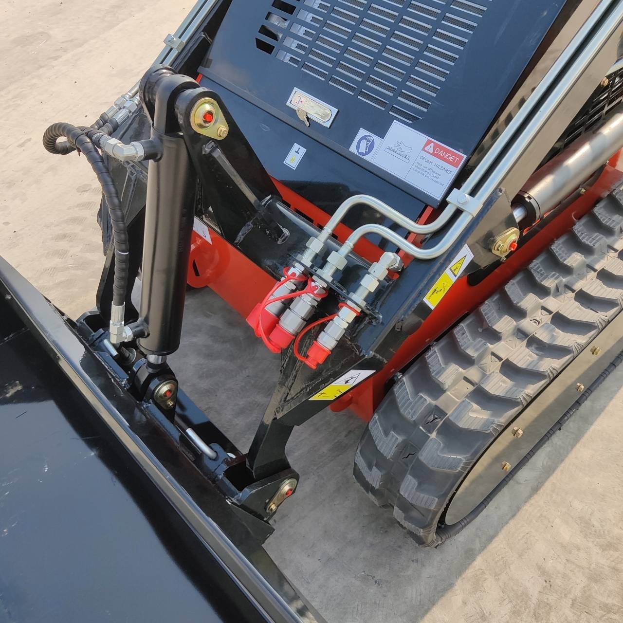 Close-up of hydraulic hoses, fittings and a cylinder on a heavy construction machine, with a large treaded tire visible nearby.