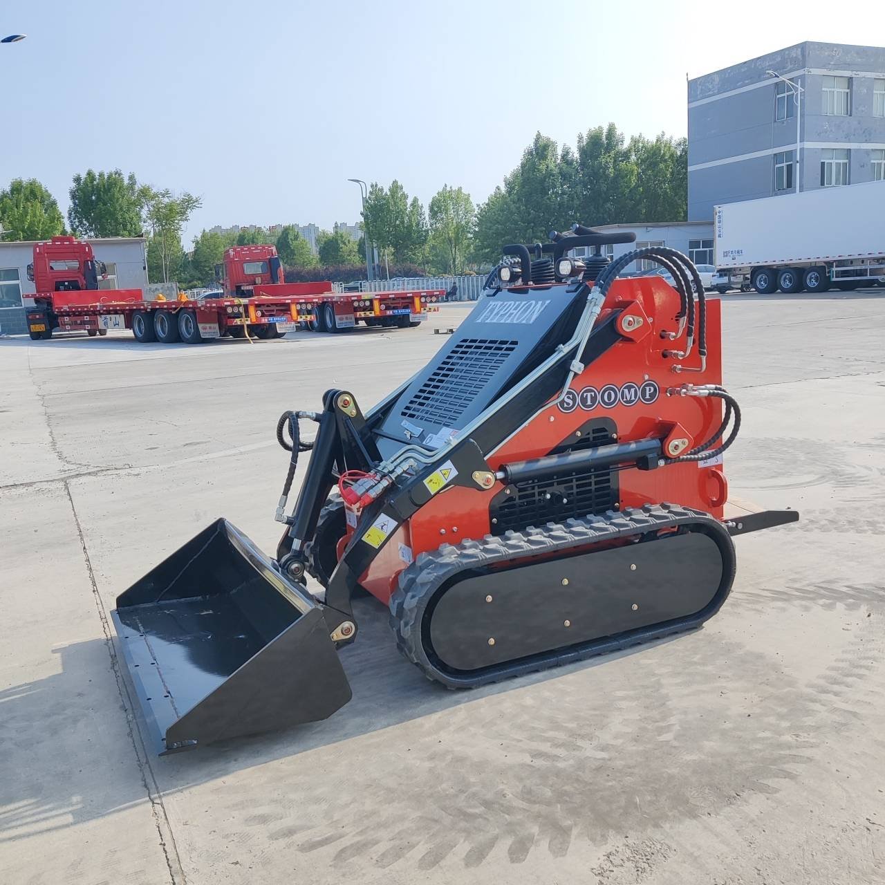 Red and black mini excavator with a front bucket on caterpillar tracks, parked in a truck yard.