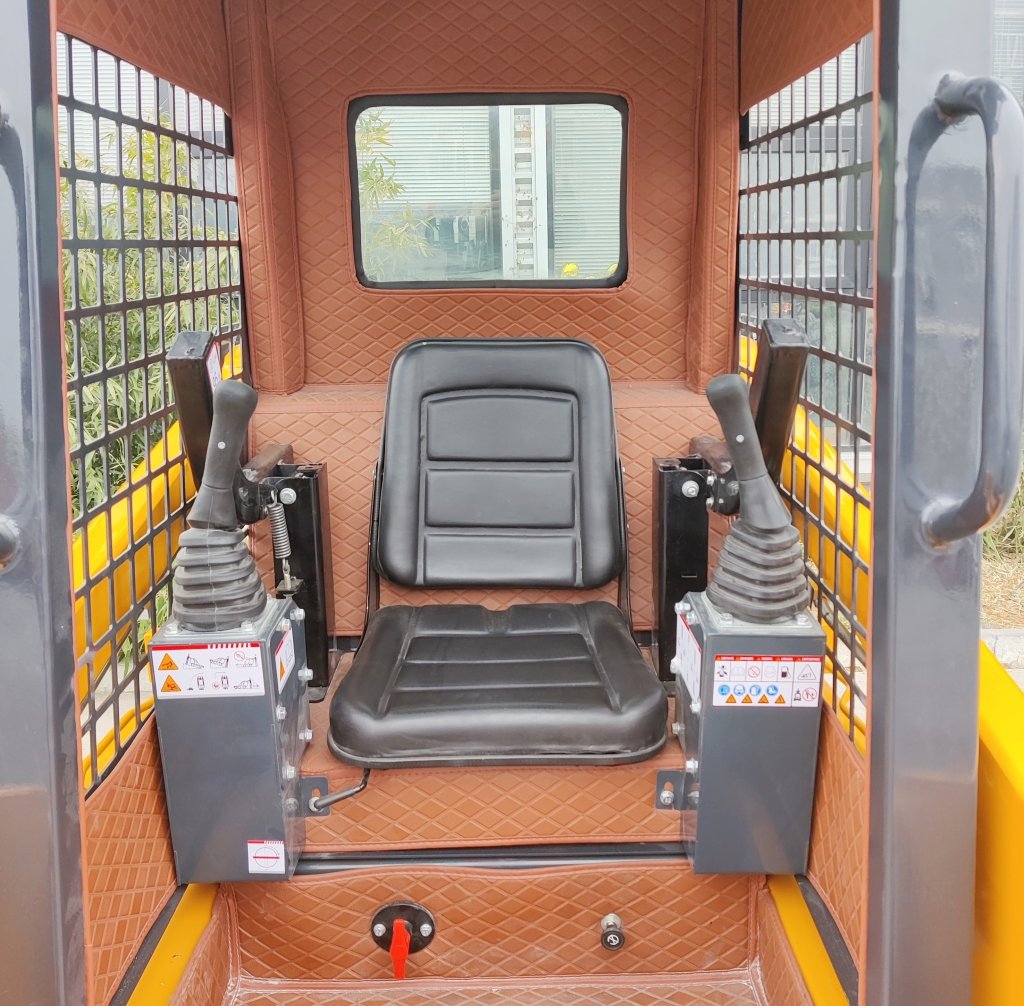 Operator seat inside a protective cab of a small excavator, with two joysticks on either side and brown quilted walls