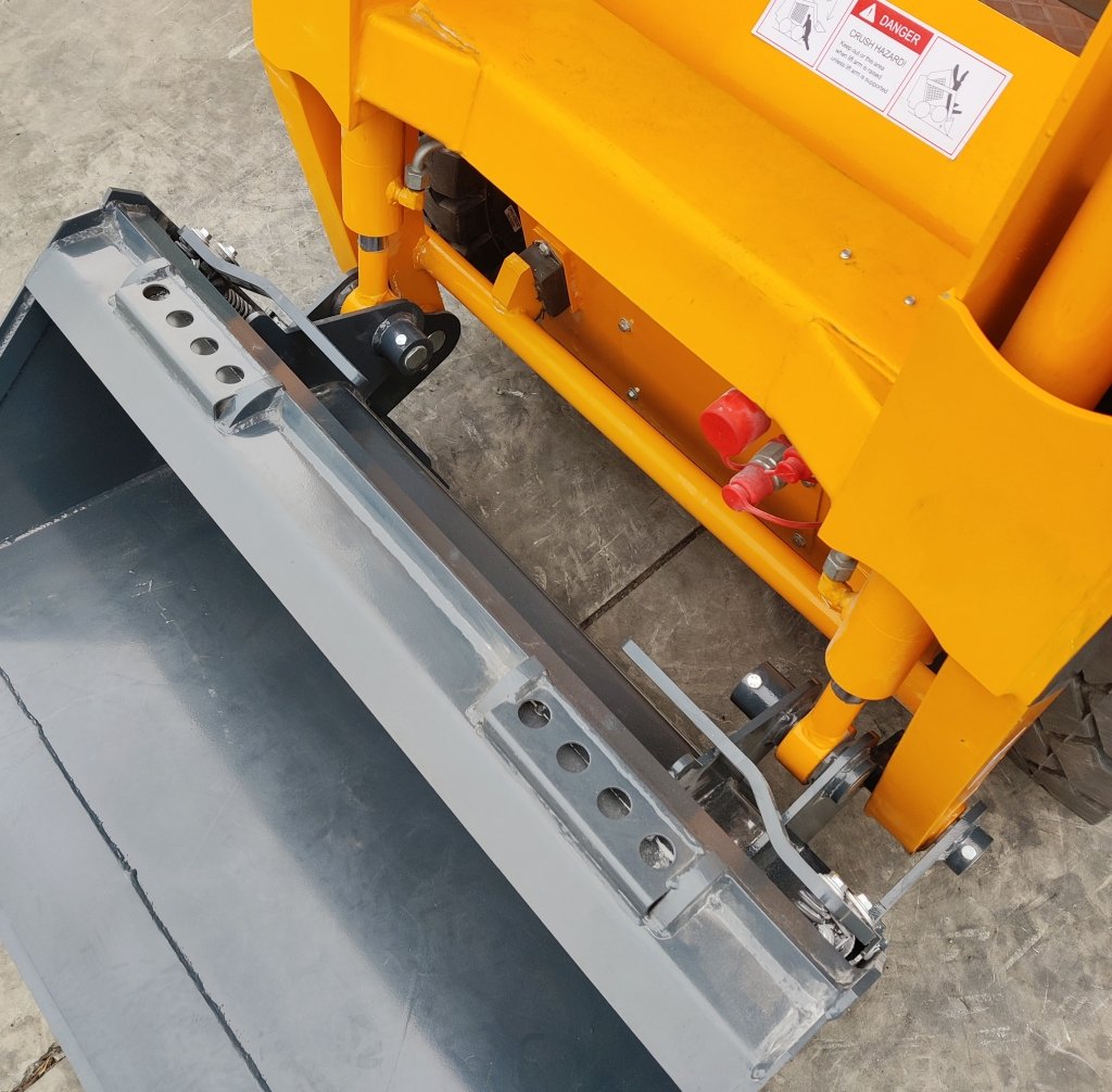 Close-up of a yellow construction machine's hydraulic arm and gray bucket, showing cylinders, pins, and a warning sticker.