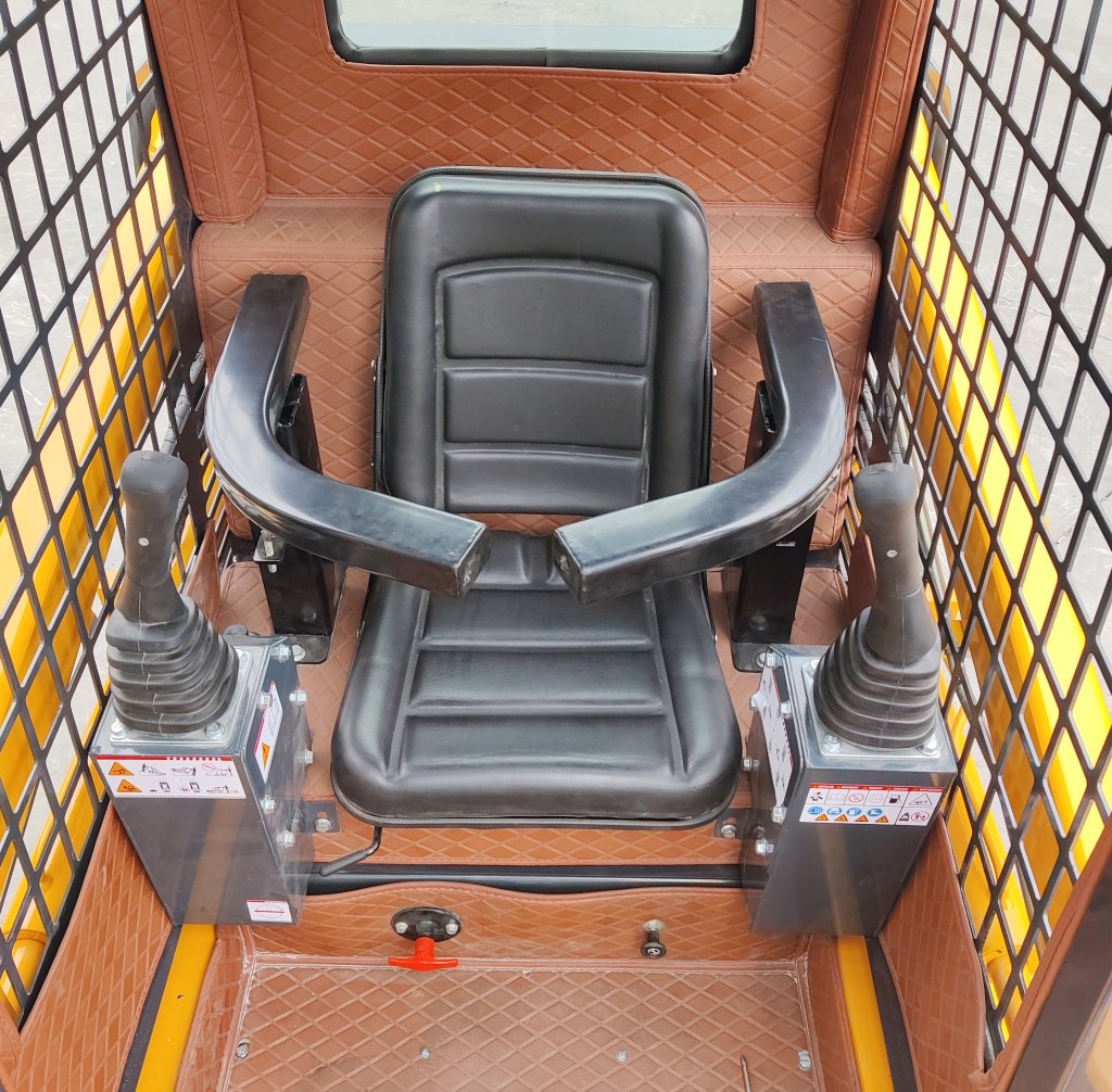 Operator seat in a skid-steer loader cab with dual joysticks on either side and a protective metal grid nearby.
