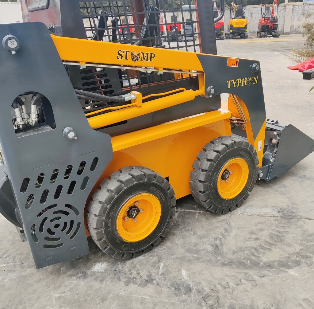 Compact skid-steer loader with yellow body and gray frame, four rugged tires, and a front bucket.