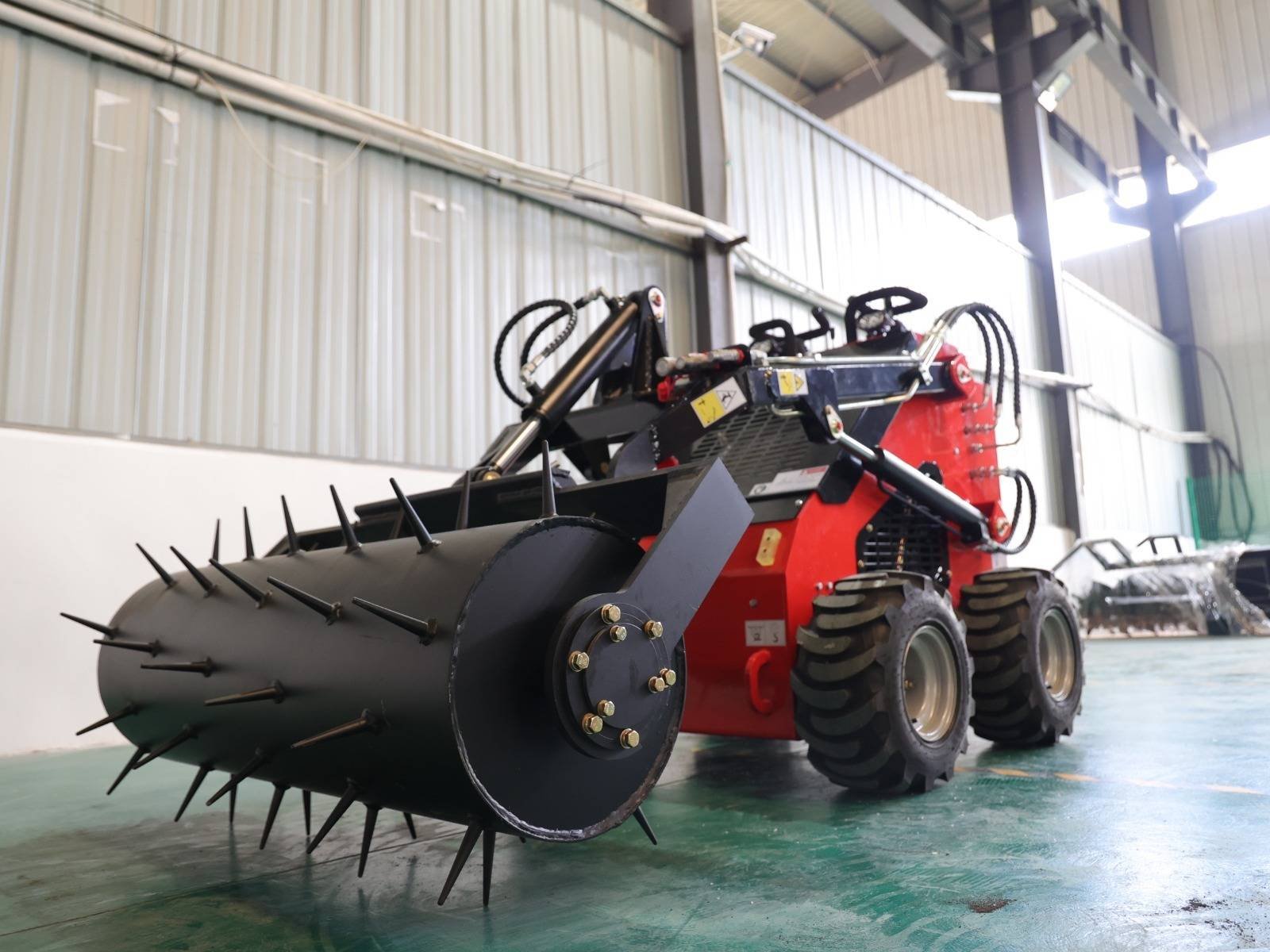 Agricultural implement with large spiked roller attached to a red machine inside a warehouse.