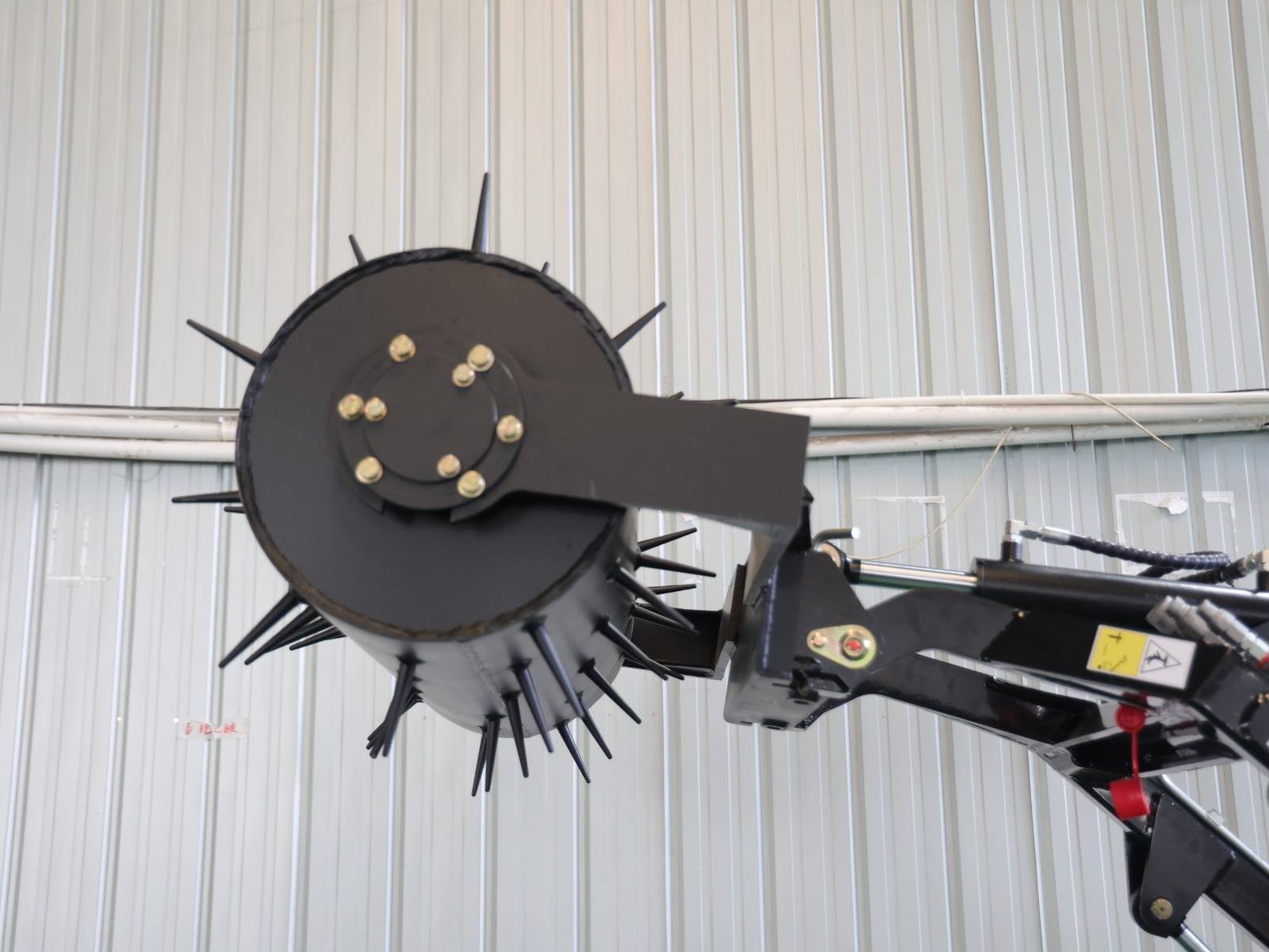 Large black circular rotary disc with spike blades mounted on an industrial arm inside a metal-walled workshop/garage.