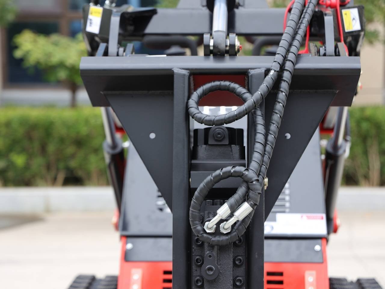 Close-up of a hydraulic arm attachment on a red construction machine, with bundled hoses and metal joints in the center.