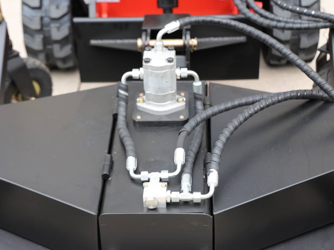 Close-up of hydraulic hose assembly with metal fittings connected to a valve on a black machinery surface.