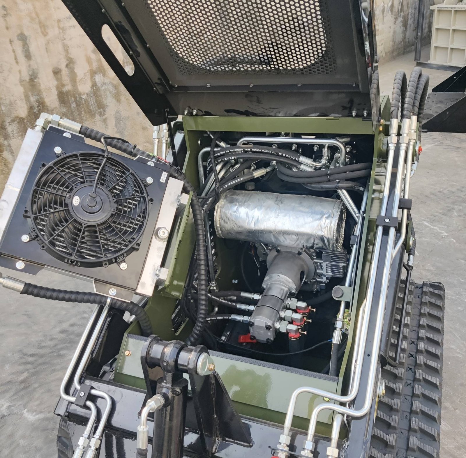 Industrial hydraulic machine internals: visible hoses, metal framing, and a cooling fan mounted on green equipment.