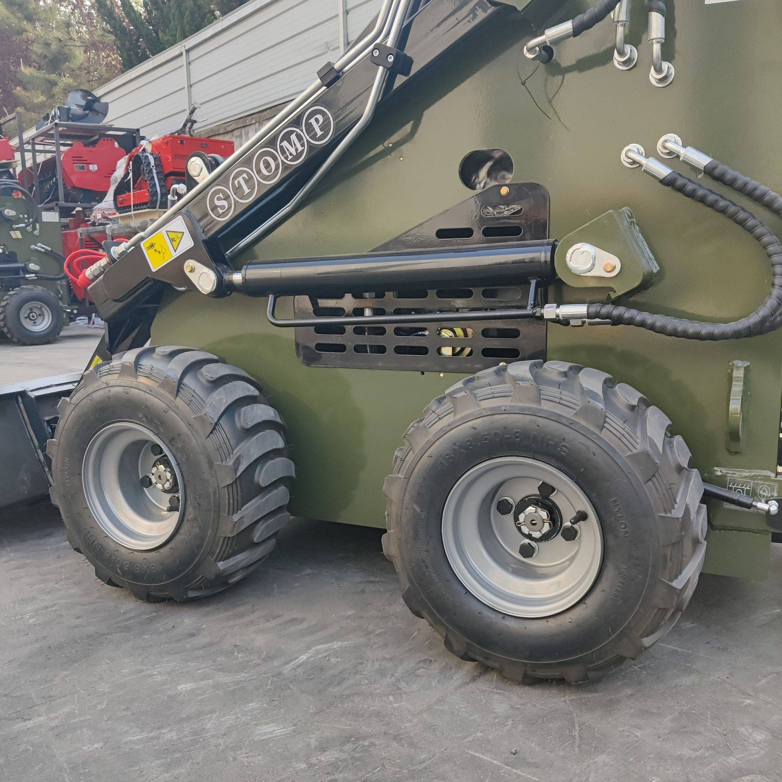 Close-up of oversized off-road tires and hydraulic linkages on a green heavy construction machine in an outdoor yard.