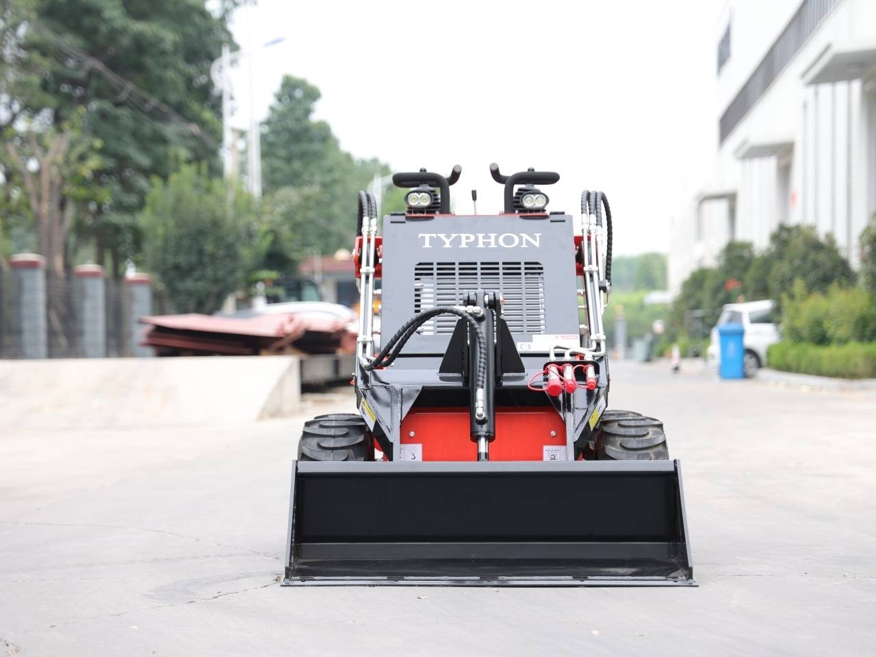 Front view of a Typhon skid-steer loader with a wide black bucket, ready for operation on a paved lot.