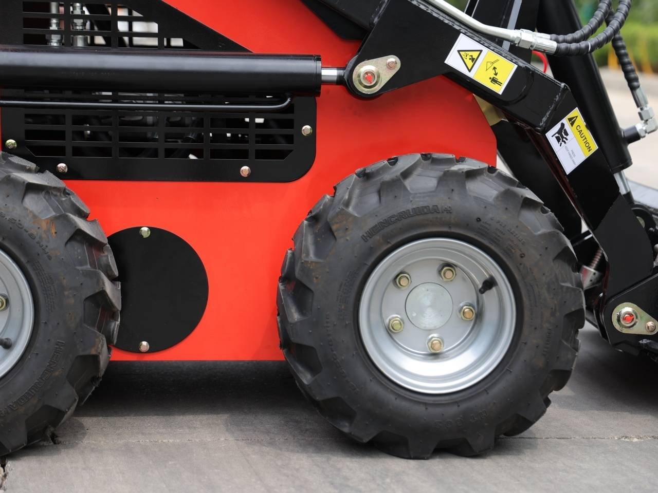Close-up of an orange industrial forklift with large rugged tires and warning decals on the arms above the wheels