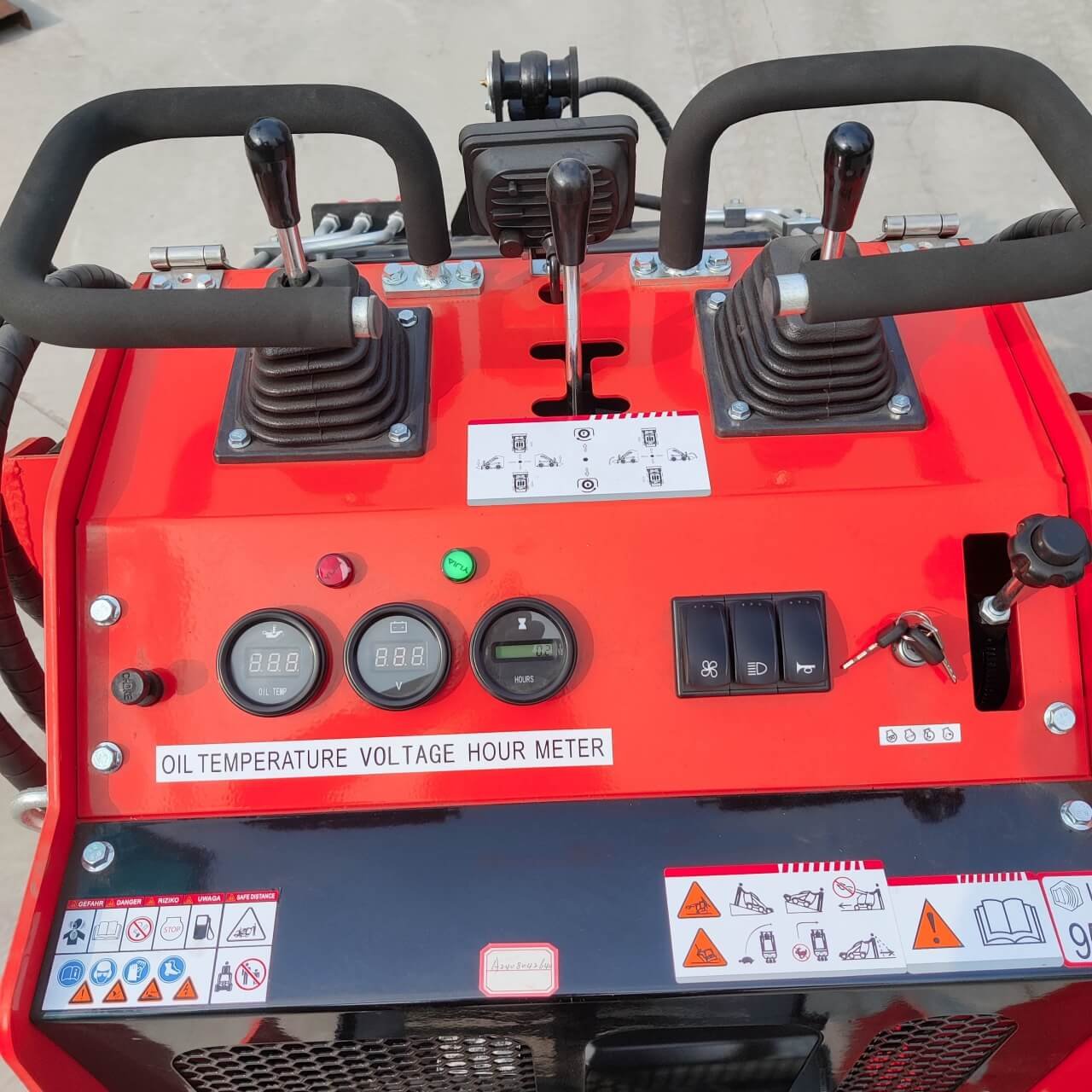 Control console of a red heavy machinery with two joystick levers, gauge clusters, and switch panel labeled for oil temp, voltage, and hour meter.
