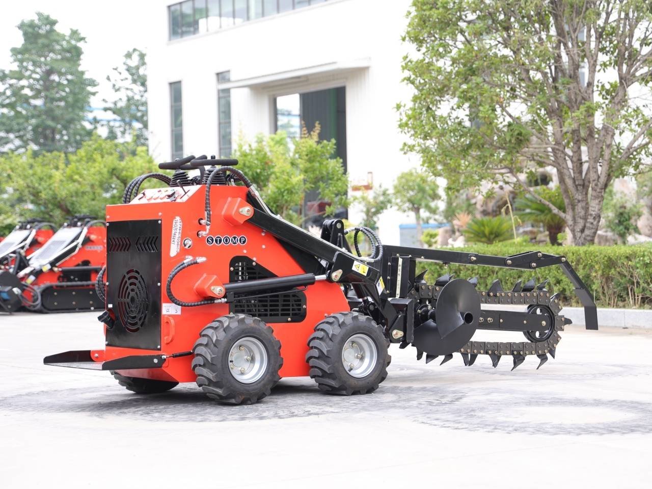 Red compact tracked trenching machine with a large auger attachment, parked on a paved lot.